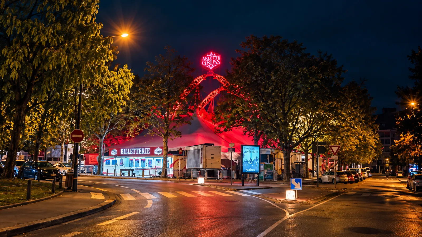 Le chapiteau illuminé du cirque Arlette Gruss installé en pleine ville, la nuit, à un carrefour, avec sa billetterie au bord de la route